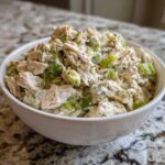 Close-up of creamy dill pickle chicken salad with chunks of chicken and green pickle pieces in a white bowl.
