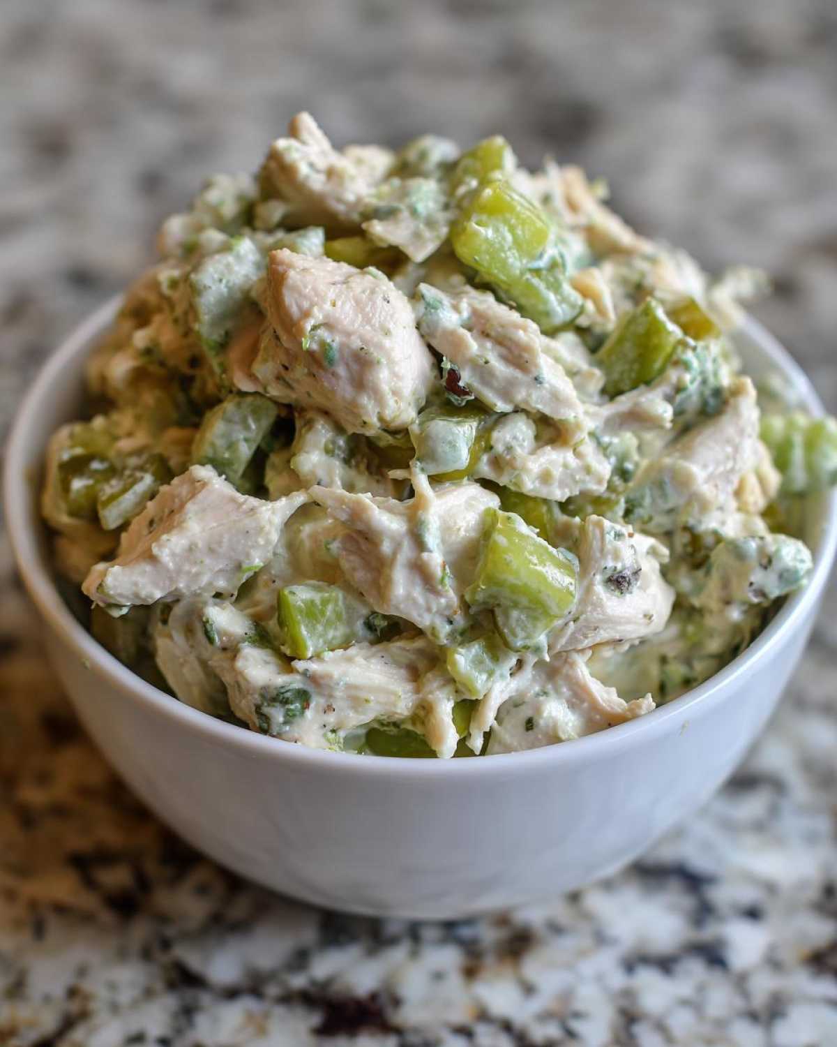 Close-up of creamy dill pickle chicken salad with chunks of chicken and bright green pickles in a white bowl.