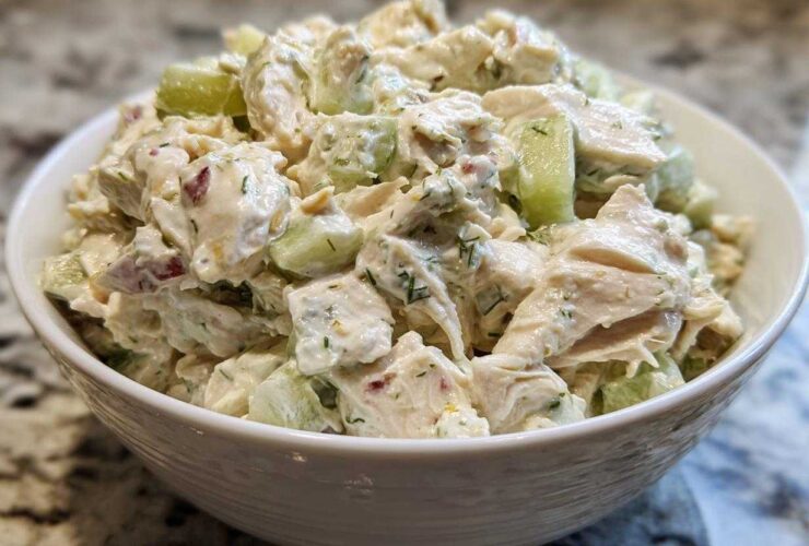 A close-up view of creamy dill pickle chicken salad, featuring chunks of chicken and cucumber, served in a white bowl.