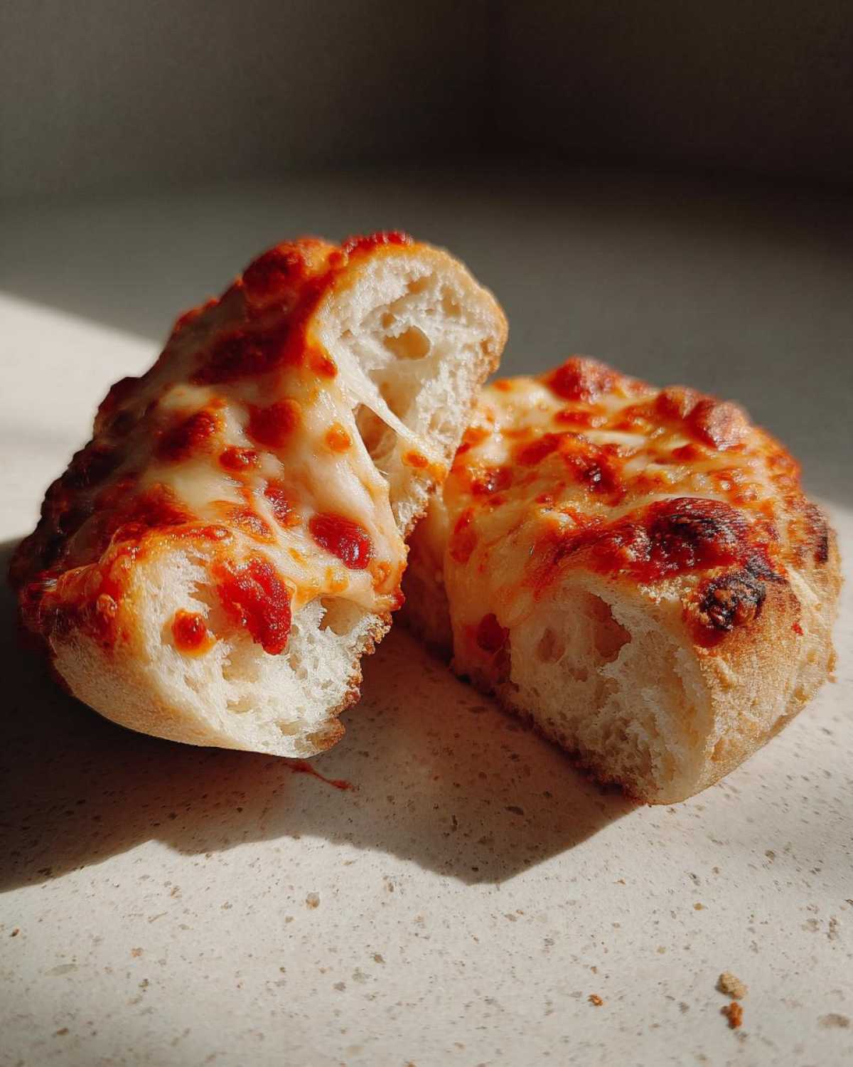 Close-up of an English muffin pizza cut in half, showing melted, stretching cheese and tomato sauce.
