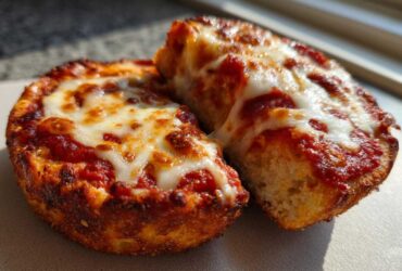 Two halves of a freshly baked English muffin pizza showing bubbly, melted mozzarella cheese over rich tomato sauce.