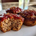 Close-up of three baked mini meatloaf portions topped with ketchup glaze, one showing the moist interior.