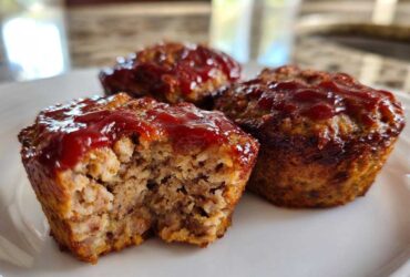Close-up of three baked mini meatloaf portions topped with ketchup glaze, one showing the moist interior.