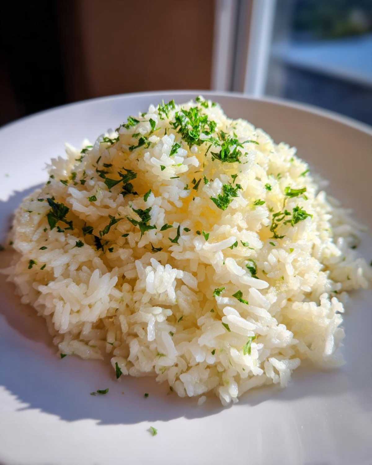A mound of fluffy white butter rice seasoned and topped with finely chopped green parsley on a white plate.