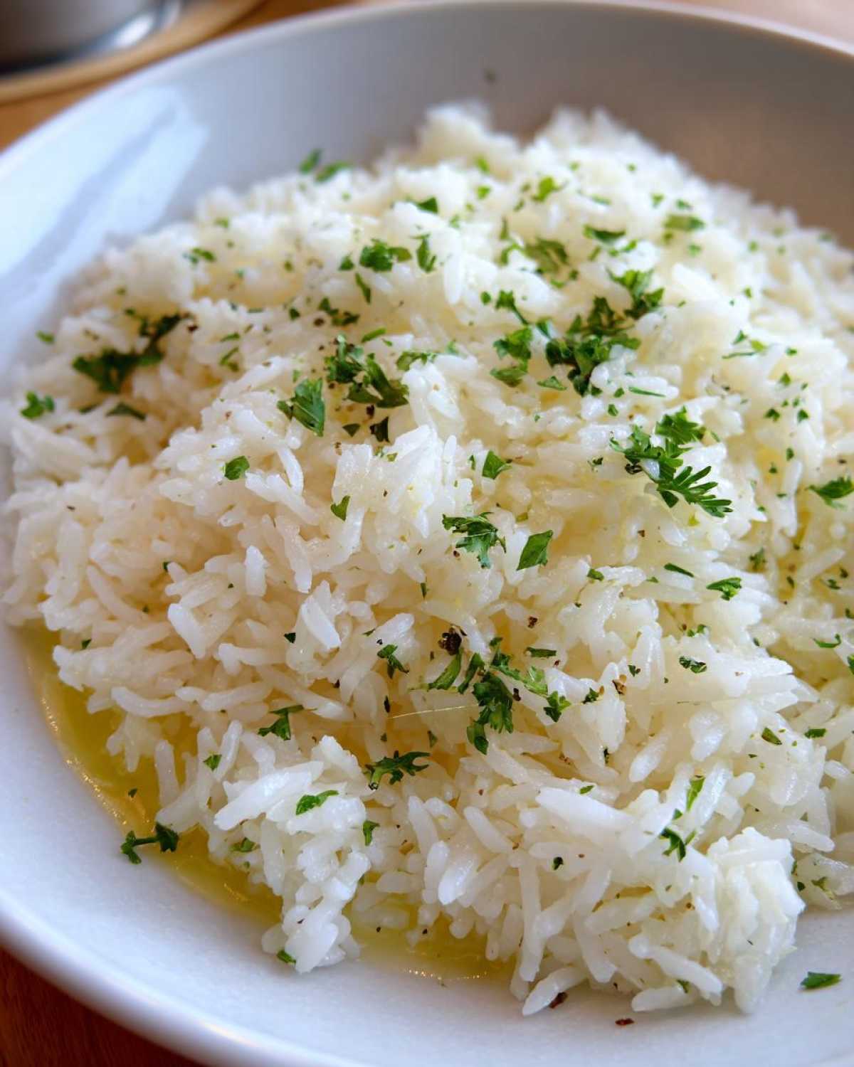 Close-up of fluffy white butter rice in a bowl, glistening with melted butter and sprinkled with chopped parsley.