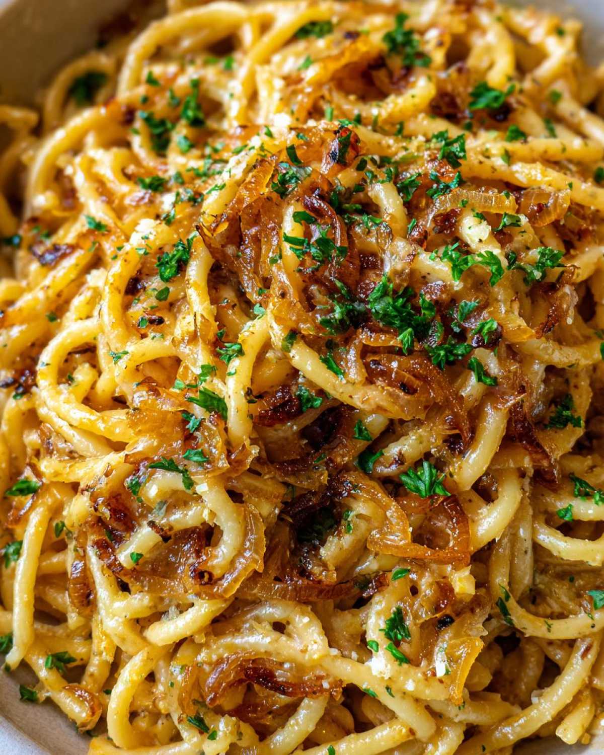 Close-up of creamy french onion pasta topped with deeply caramelized onions and fresh parsley.