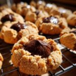 Close-up of a freshly baked peanut butter blossom cookie with a dollop of melted chocolate on a wire cooling rack.