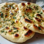 Two pieces of freshly baked naan bread brushed with melted butter and topped with chopped parsley.