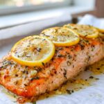 Close-up of a perfectly cooked garlic butter salmon fillet topped with fresh lemon slices and herbs.