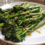 Close-up of perfectly cooked, bright green broccolini topped with crispy garlic bits on a white plate.