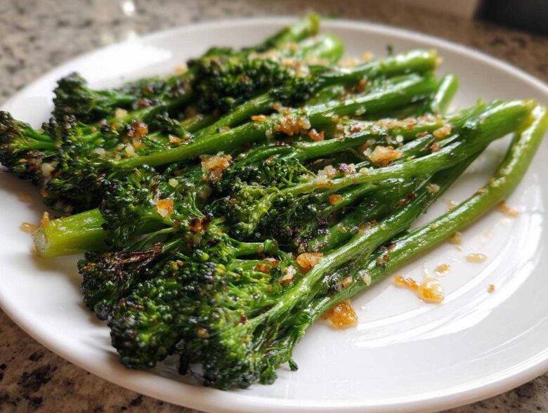 Close-up of perfectly cooked, bright green broccolini topped with crispy garlic bits on a white plate.