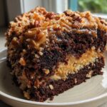Close-up of a rich slice of german chocolate poke cake showing dark chocolate layers and coconut pecan frosting.