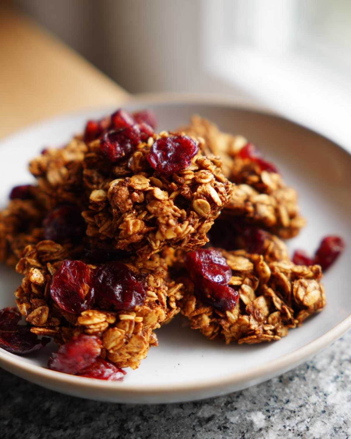 Close-up of crunchy gingerbread granola clusters topped with bright red dried cranberries on a white plate.