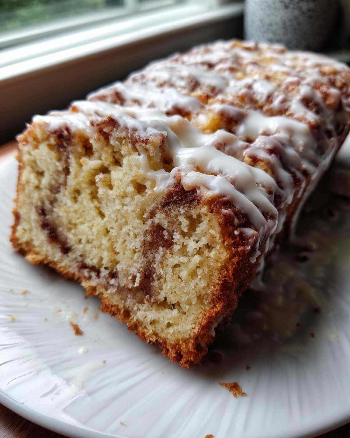 A close-up view of a freshly baked apple fritter bread loaf drizzled heavily with white icing.