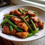 Close-up of glossy, saucy chicken and bright green beans, showcasing the delicious chicken and green beans dish.
