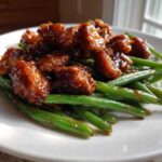 Close-up of glazed chicken pieces served over bright green beans, showcasing the delicious chicken and green beans dish.
