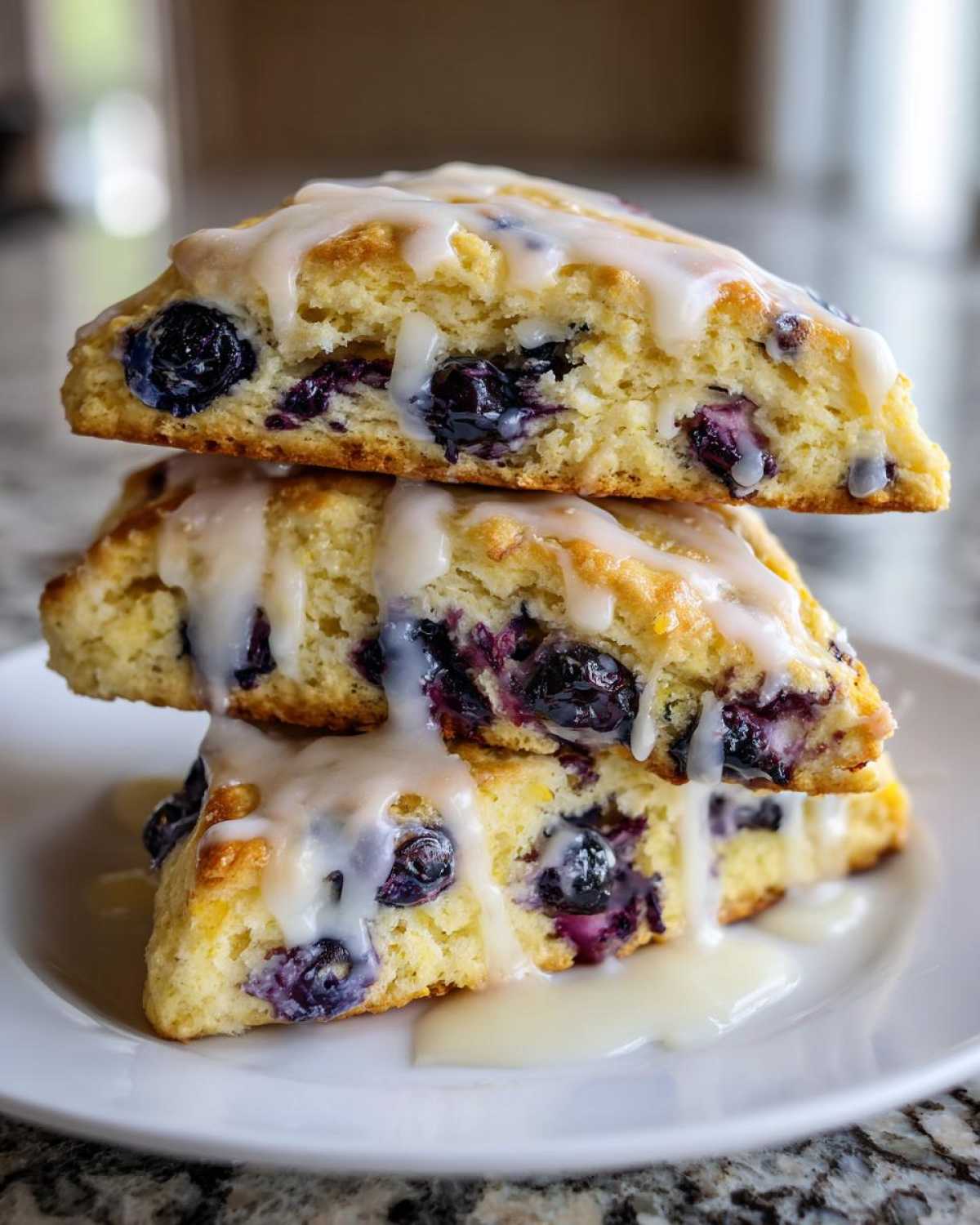Three lemon blueberry scones stacked and drizzled with a thick, white lemon glaze.