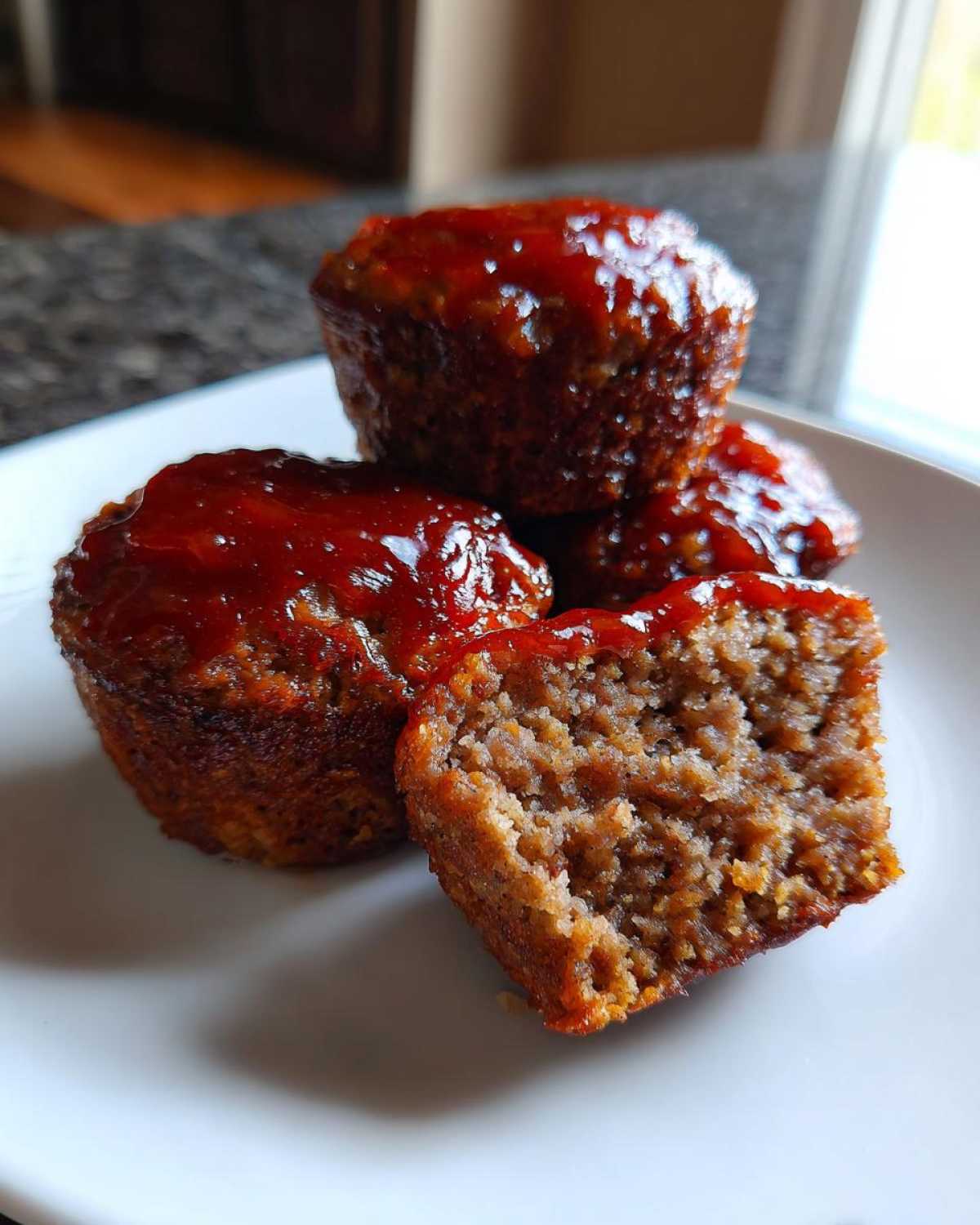 Three glazed mini meatloaf portions stacked on a white plate, one cut open showing the texture.