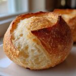 Close-up of a perfectly baked, round bread bowl with a golden, crusty exterior and soft interior.