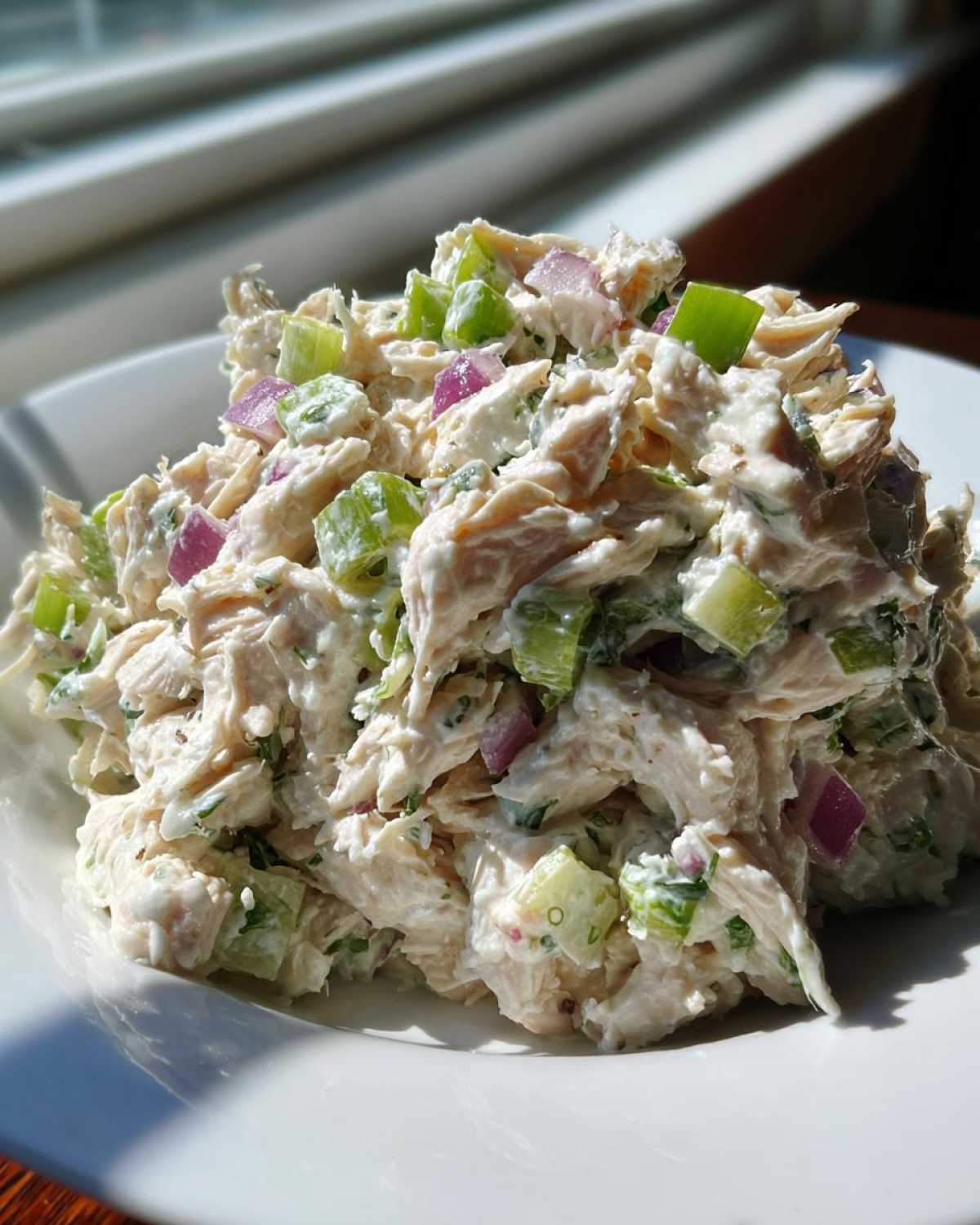 Close-up of creamy greek yogurt chicken salad mixed with diced celery and red onion on a white plate.
