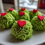 Six festive grinch oreo balls covered in green frosting strands and topped with small red hearts.