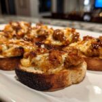 Close-up of cheesy, savory hanky panky recipe topping served on toasted baguette slices.