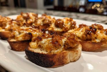 Close-up of cheesy, savory hanky panky recipe topping served on toasted baguette slices.