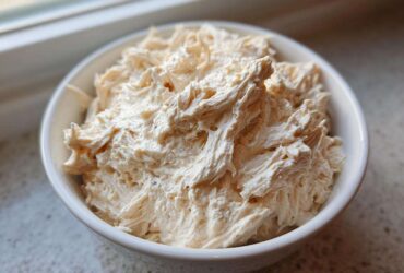 Close-up of fluffy, shredded chicken mixed into a creamy base, representing homemade cream of chicken soup.