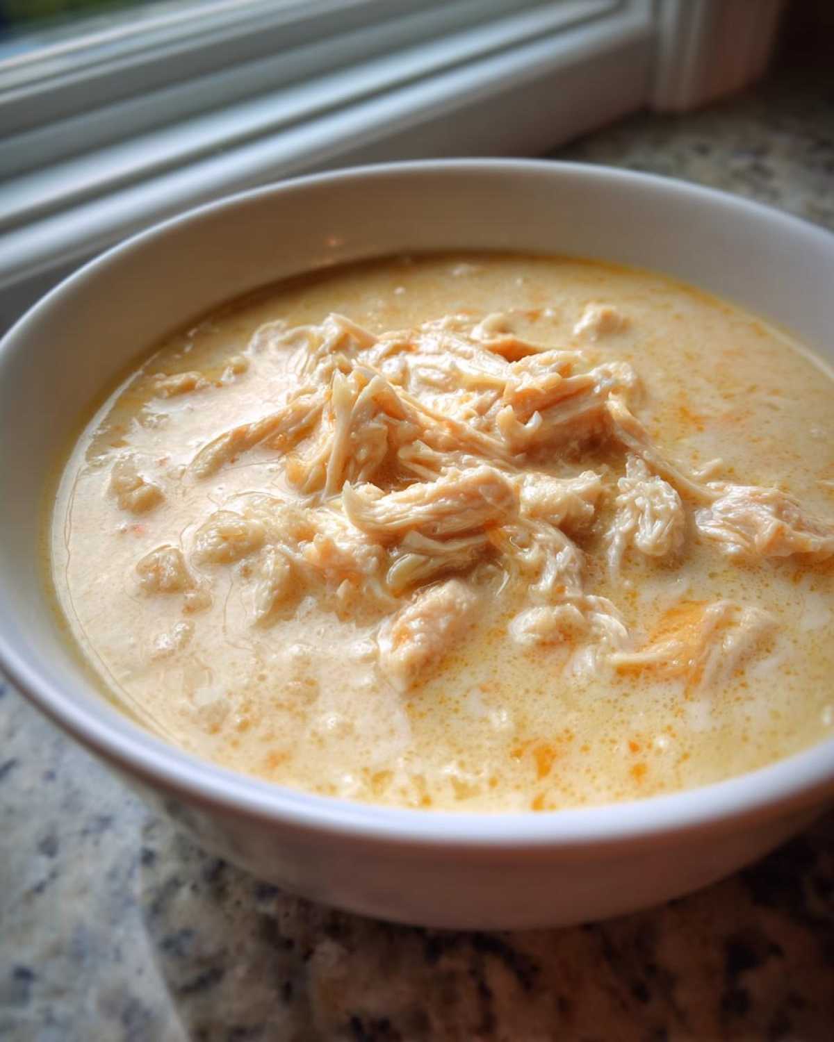Close-up of a white bowl filled with creamy, homemade cream of chicken soup topped generously with shredded chicken.