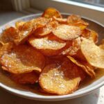 A bowl piled high with golden brown, homemade potato chips sprinkled with coarse salt.