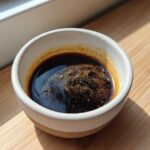 Close-up of rich, dark homemade teriyaki sauce with spices floating on top in a small ceramic bowl.