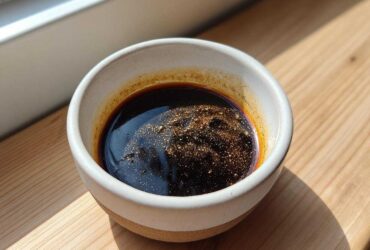 Close-up of rich, dark homemade teriyaki sauce with spices floating on top in a small ceramic bowl.