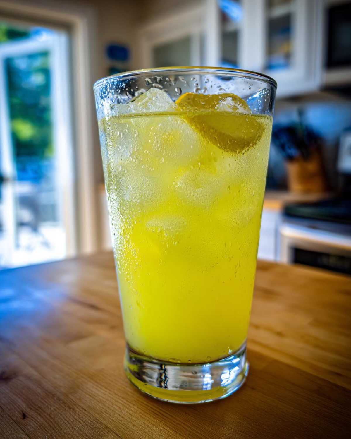 A tall, sweating glass filled with bright yellow iced lemonade and a lemon slice garnish.