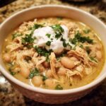 A close-up of a bowl filled with creamy instant pot white chicken chili, topped with sour cream and fresh parsley.