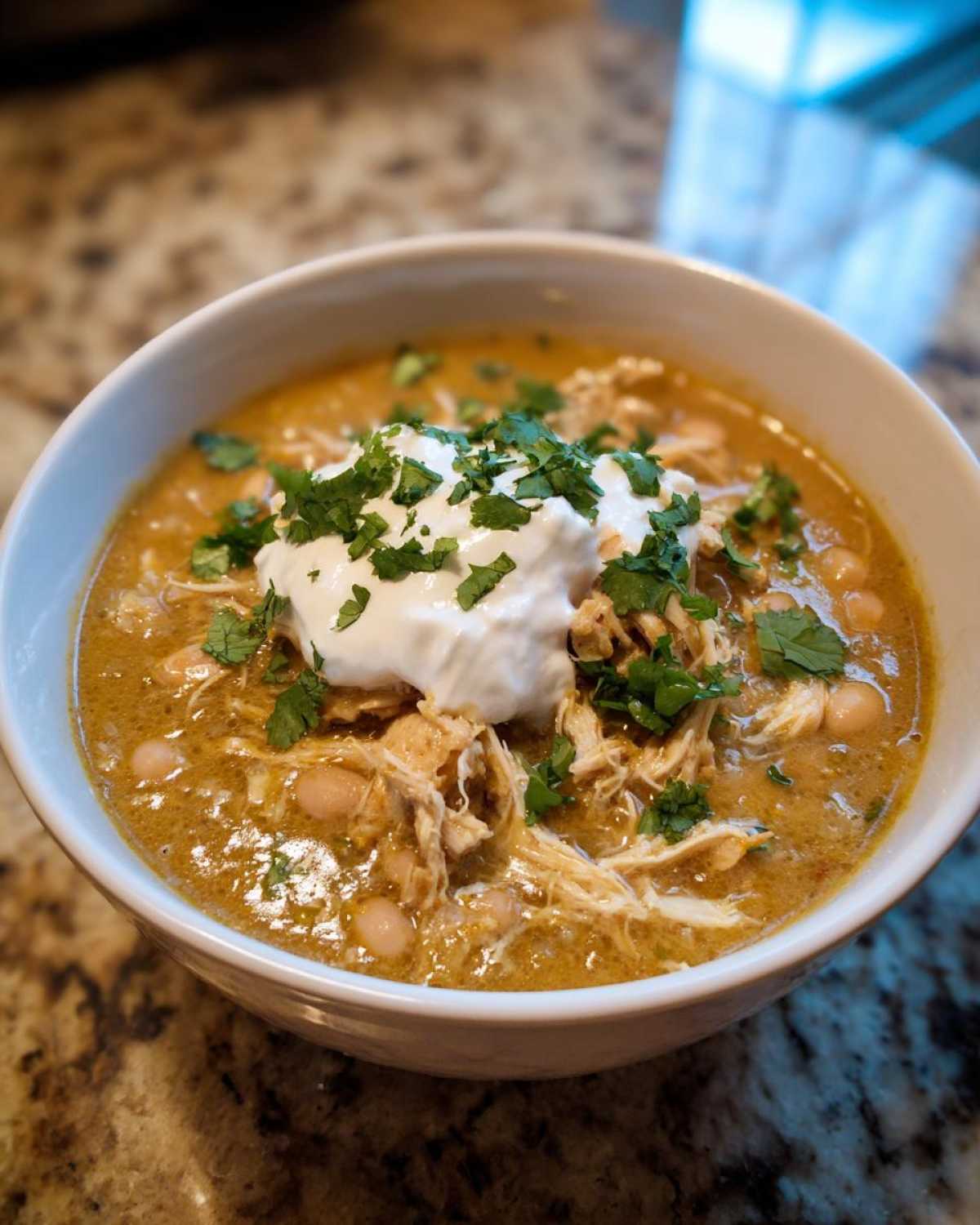 A close-up of a white bowl filled with creamy instant pot white chicken chili, topped with sour cream and fresh cilantro.
