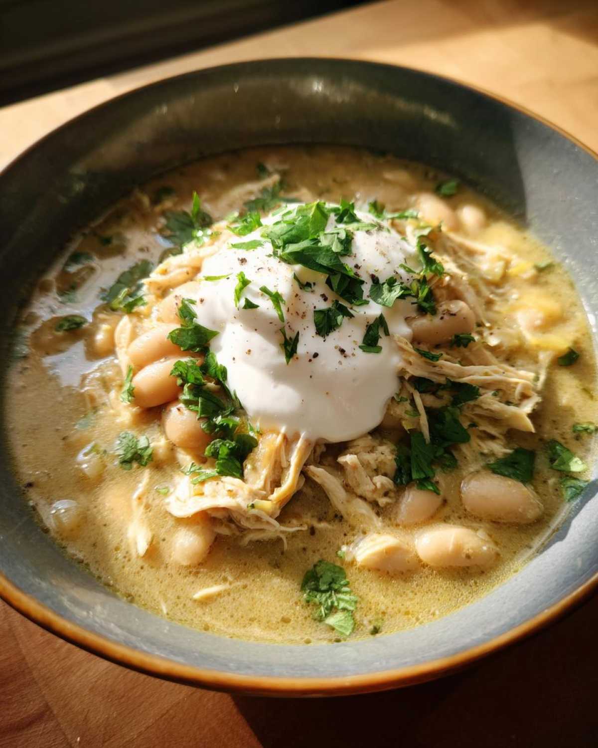 Close-up of a bowl of instant pot white chicken chili topped with sour cream, fresh cilantro, and pepper.