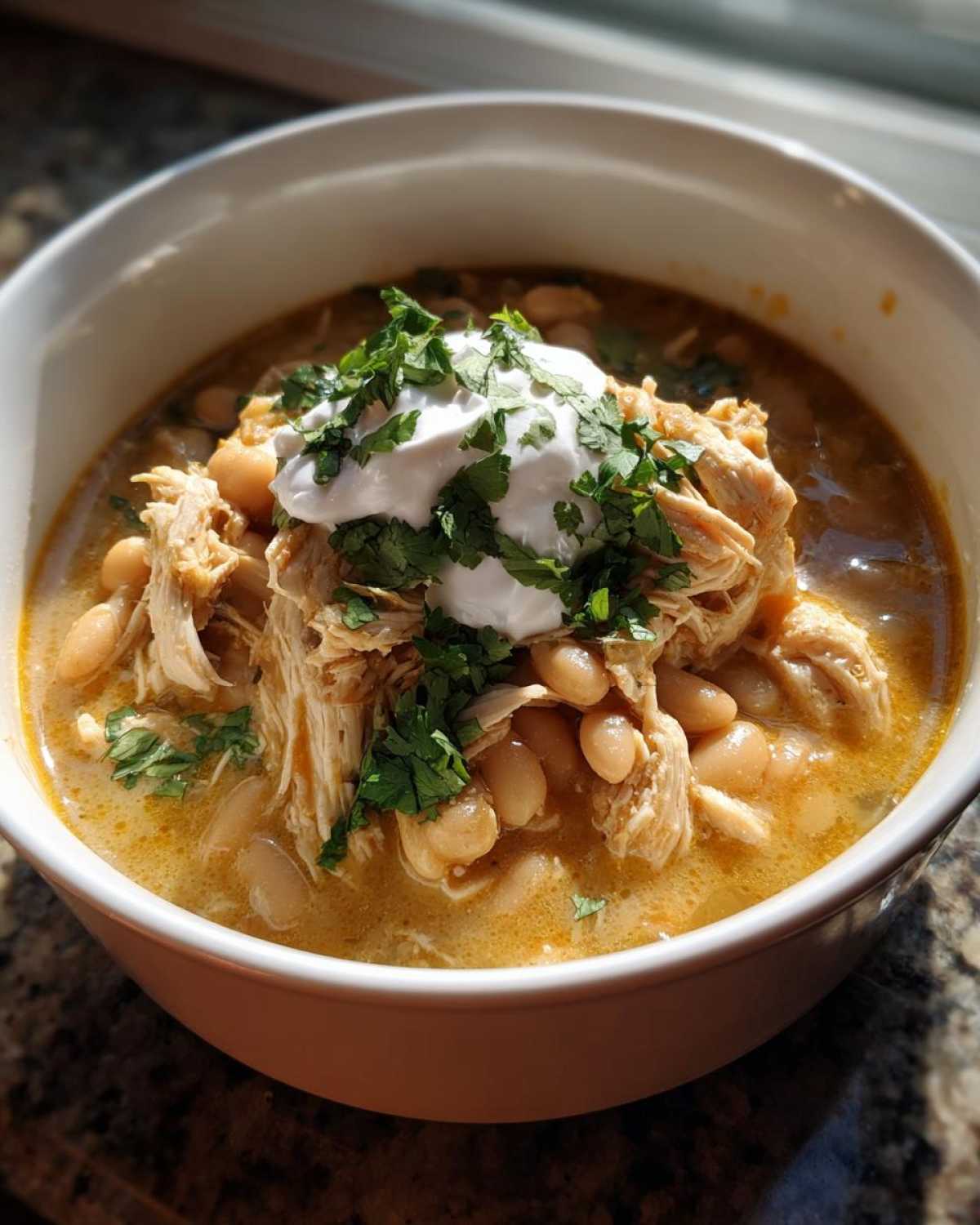 Close-up of a bowl of instant pot white chicken chili topped with shredded chicken, white beans, sour cream, and cilantro.