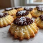 Close-up of several piped Italian butter cookies topped with dark chocolate frosting and powdered sugar.