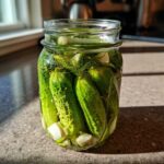 A glass jar filled with crisp cucumbers, dill sprigs, and garlic cloves for making refrigerator pickles.