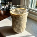 A glass jar filled with creamy, textured chia seed pudding, topped with extra seeds.