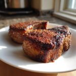 Two thick, juicy baked pork chops with a dark, flavorful crust resting on a white plate.