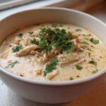 A close-up of a bowl of creamy keto white chicken chili topped with shredded chicken and fresh cilantro.