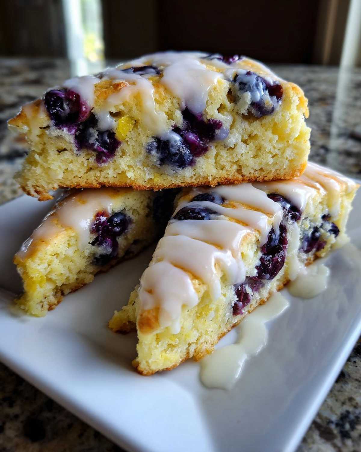 Close-up of three tender lemon blueberry scones stacked, drizzled heavily with white lemon glaze.