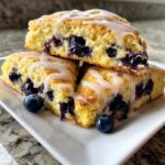 Close-up of three tender lemon blueberry scones stacked and drizzled with white glaze, garnished with fresh blueberries.