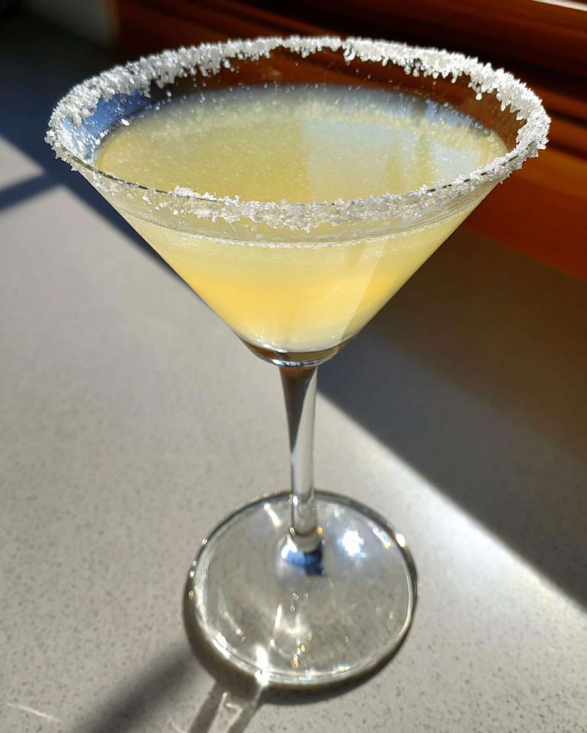 A bright yellow lemon drop cocktail served in a martini glass with a thick, sparkling sugar rim.
