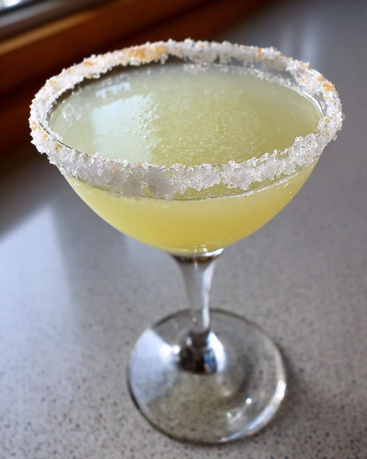 A bright yellow lemon drop cocktail served in a martini glass with a thick, sparkling sugar rim.