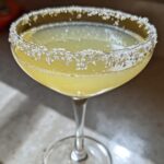 Close-up of a bright yellow lemon drop cocktail in a coupe glass with a heavily sugared rim.
