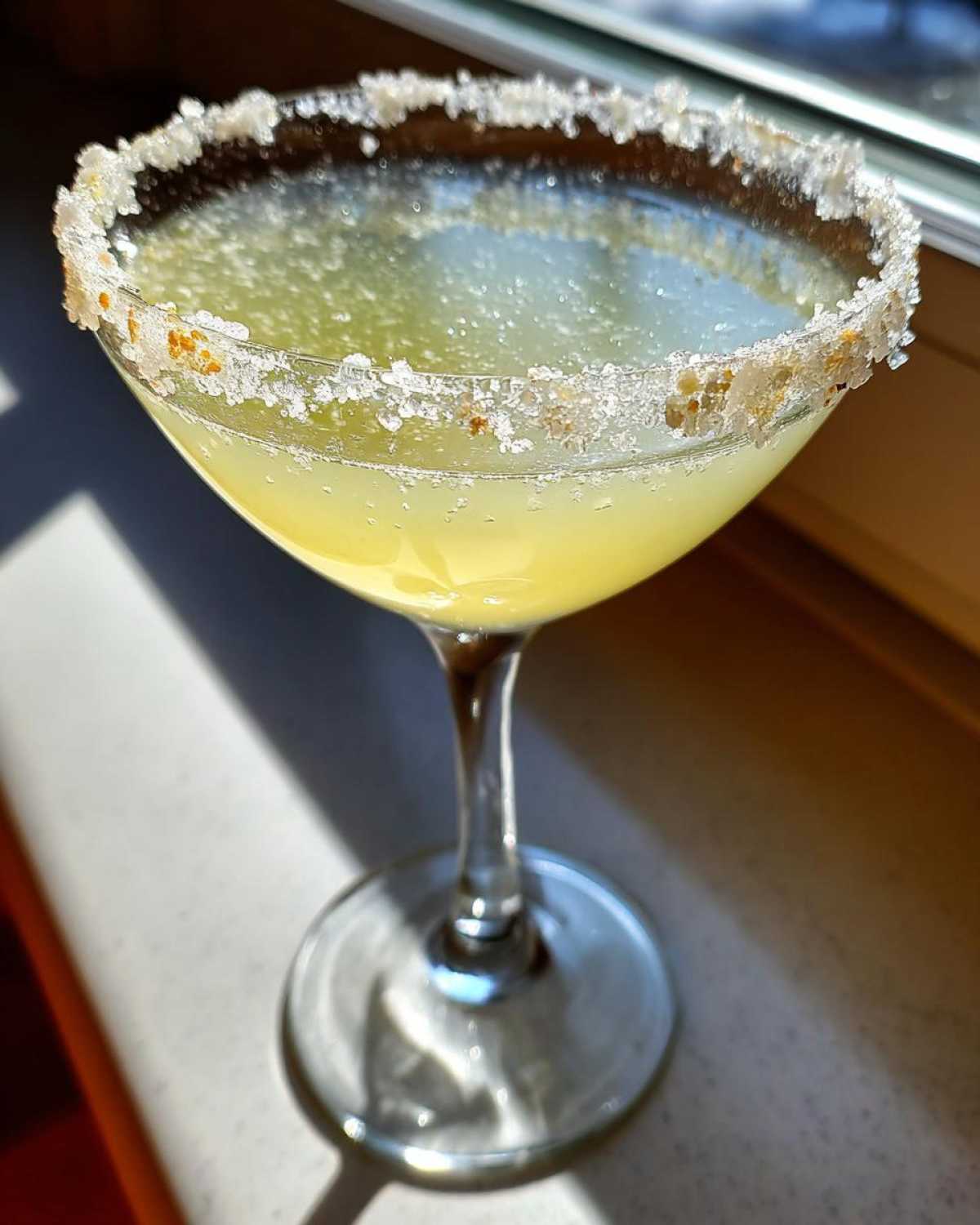 Close-up of a bright yellow lemon drop cocktail in a coupe glass with a thick, sparkling sugar rim.