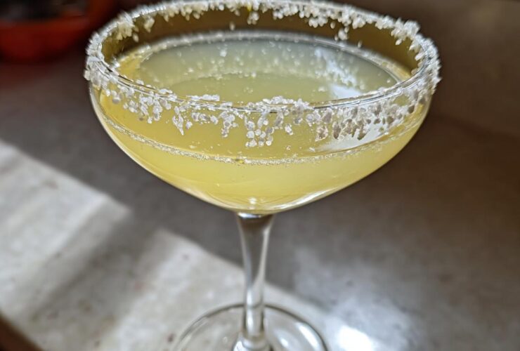 Close-up of a bright yellow lemon drop cocktail in a coupe glass with a heavily sugared rim.