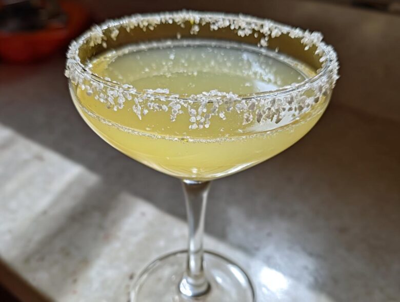 Close-up of a bright yellow lemon drop cocktail in a coupe glass with a heavily sugared rim.